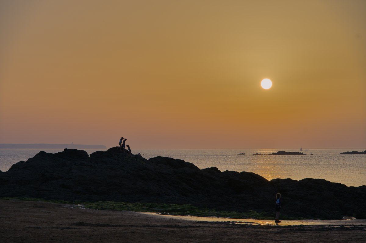 Des enfants en silhouette sur un rocher au coucher de soleil, plage de Longchamp.