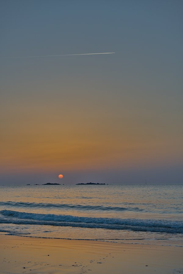 Le soleil orange se couche entre deux îlots au large de la plage de Longchamp.